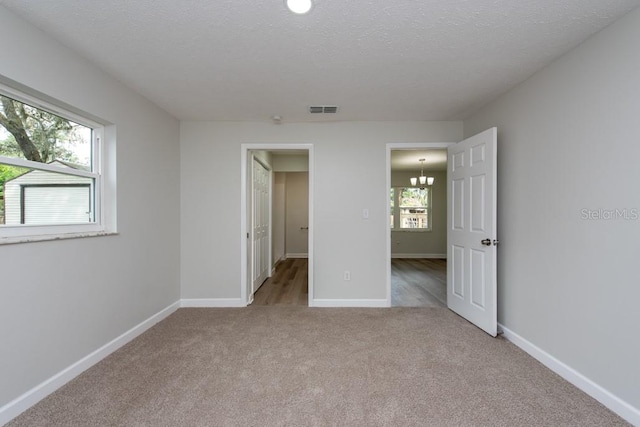 unfurnished bedroom with a notable chandelier, light colored carpet, and a textured ceiling