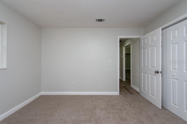 unfurnished bedroom featuring light carpet, a closet, and a textured ceiling