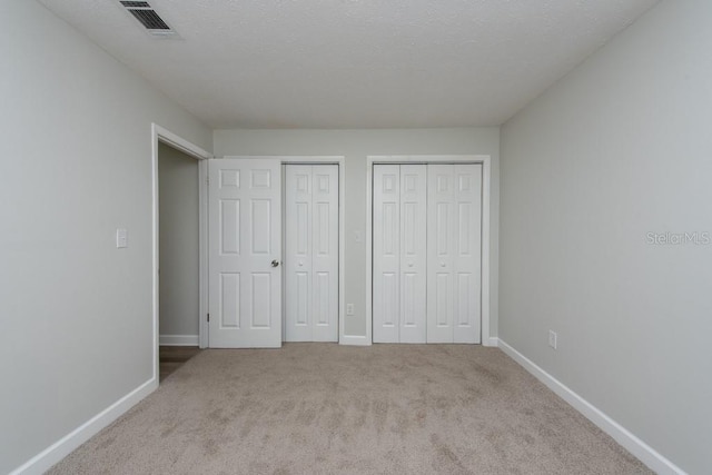 unfurnished bedroom with a textured ceiling, light carpet, and multiple closets