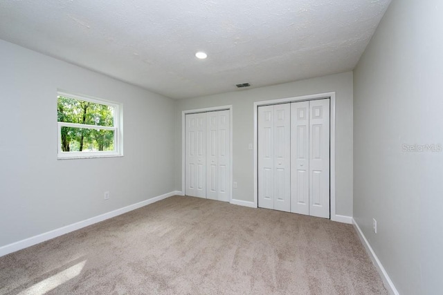 unfurnished bedroom featuring carpet, a textured ceiling, and multiple closets