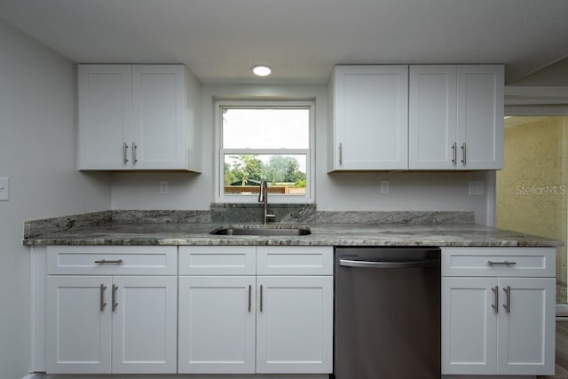 kitchen with stainless steel dishwasher, dark stone countertops, white cabinetry, and sink