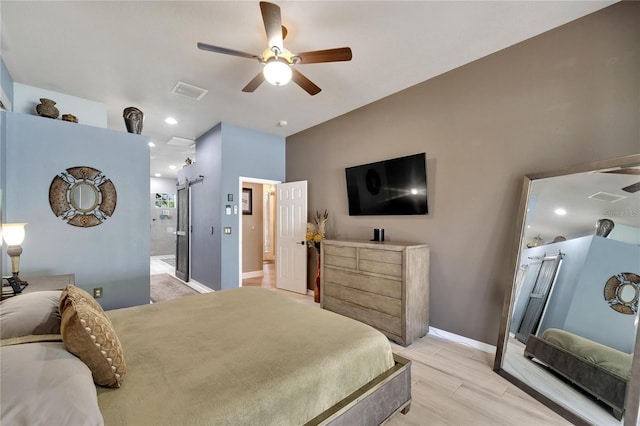 bedroom with light hardwood / wood-style flooring, ensuite bath, ceiling fan, and a barn door