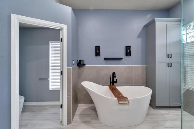 bathroom with tile walls, a bathing tub, toilet, and a wealth of natural light