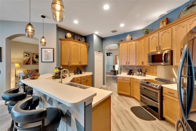 kitchen with pendant lighting, sink, backsplash, stainless steel appliances, and light hardwood / wood-style floors