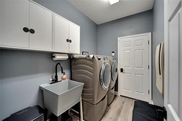 washroom featuring sink, washing machine and clothes dryer, a textured ceiling, cabinets, and light hardwood / wood-style floors