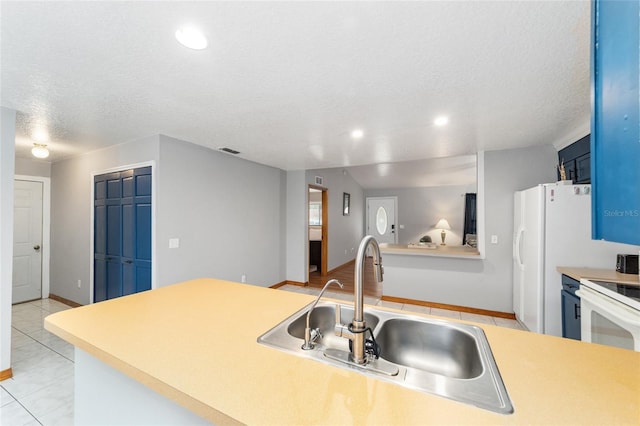 kitchen with a textured ceiling, light tile patterned floors, sink, and blue cabinetry