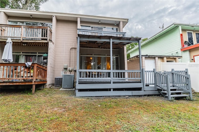 back of property featuring central AC unit, a balcony, a wooden deck, and a yard