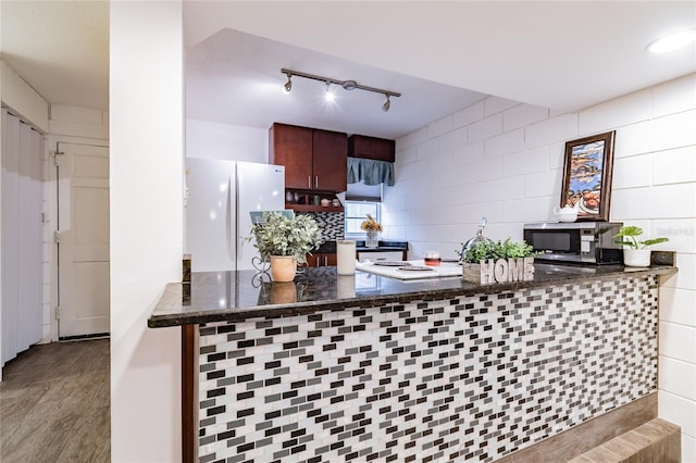 kitchen featuring dark stone counters, light wood-type flooring, kitchen peninsula, white fridge, and dark brown cabinetry