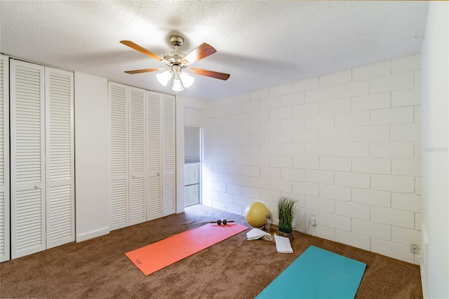 workout area featuring dark colored carpet, ceiling fan, and a textured ceiling