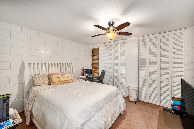 carpeted bedroom featuring ceiling fan, a textured ceiling, and multiple closets