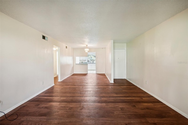 unfurnished living room with an inviting chandelier, a textured ceiling, and dark hardwood / wood-style flooring