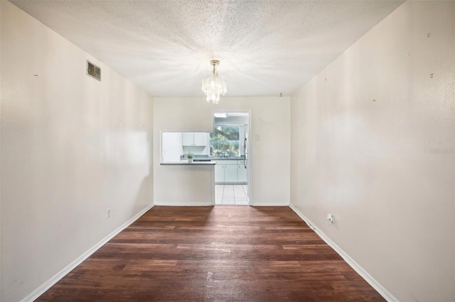 spare room with a chandelier, a textured ceiling, and dark wood-type flooring