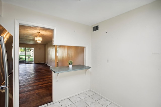 interior space featuring stainless steel refrigerator, kitchen peninsula, a breakfast bar area, light hardwood / wood-style flooring, and a notable chandelier