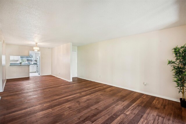 unfurnished living room featuring a textured ceiling, a chandelier, and dark wood-type flooring