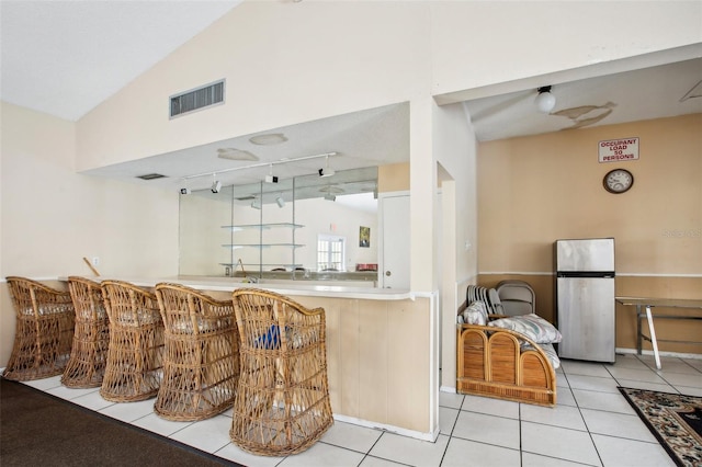 bar with stainless steel refrigerator, lofted ceiling, light tile patterned flooring, and rail lighting