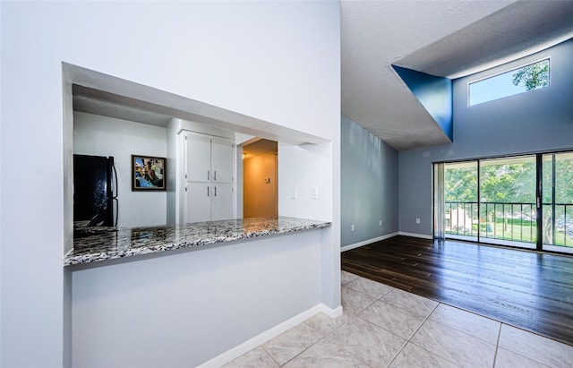 kitchen with light hardwood / wood-style floors, stone countertops, black fridge, and plenty of natural light