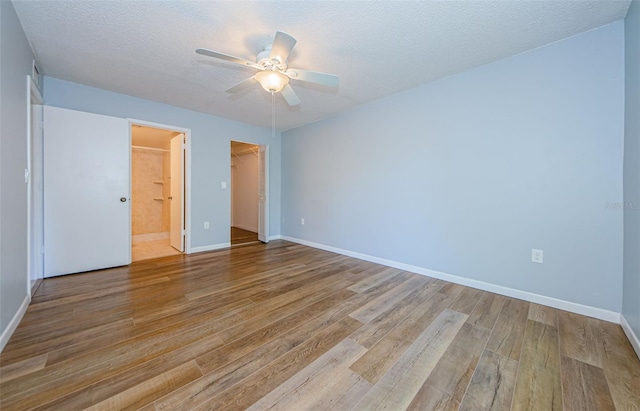 unfurnished bedroom with light wood-type flooring, a closet, a textured ceiling, a spacious closet, and ceiling fan