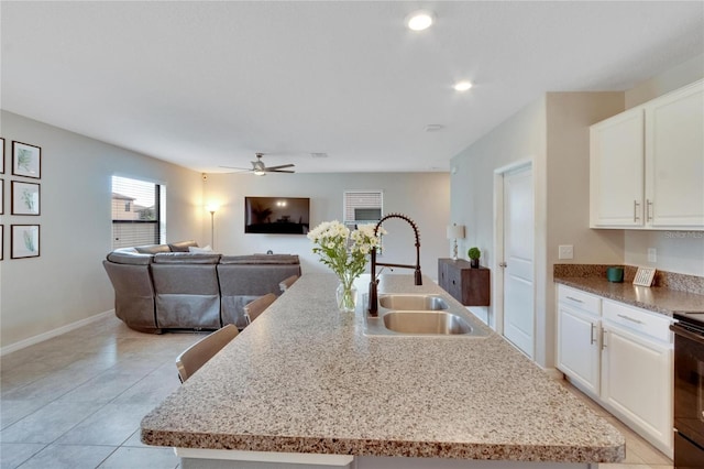 kitchen with ceiling fan, white cabinetry, sink, and an island with sink