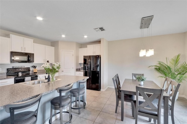 kitchen featuring light tile patterned flooring, black appliances, pendant lighting, white cabinets, and an island with sink