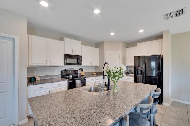 kitchen with light tile patterned flooring, sink, a kitchen island with sink, and black appliances