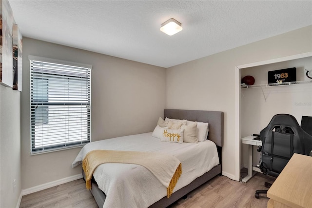 bedroom with light hardwood / wood-style floors, a textured ceiling, and a closet