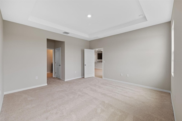 unfurnished bedroom featuring light colored carpet and a raised ceiling