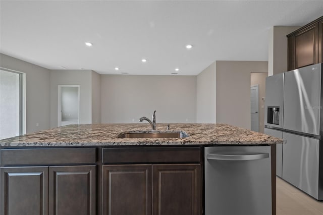 kitchen featuring dark stone countertops, stainless steel appliances, dark brown cabinets, a kitchen island with sink, and sink