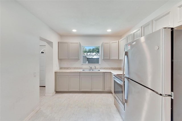kitchen with light countertops, recessed lighting, gray cabinetry, a sink, and appliances with stainless steel finishes