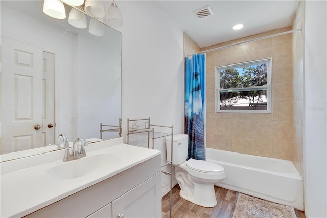 bathroom featuring visible vents, toilet, wood finished floors, vanity, and shower / bath combo with shower curtain