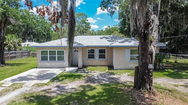 view of front of property with concrete block siding, roof with shingles, a front yard, and fence