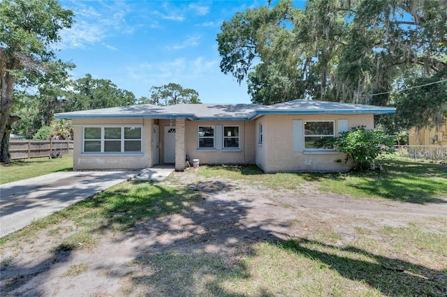 view of front facade with concrete block siding, driveway, fence, and a front lawn