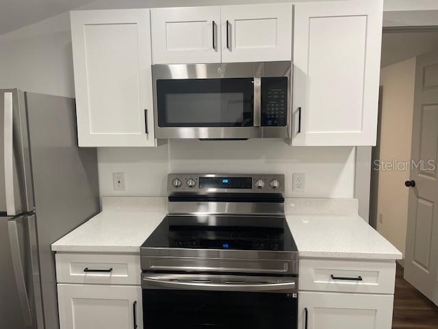 kitchen with stainless steel appliances, white cabinets, dark wood-type flooring, and light stone counters