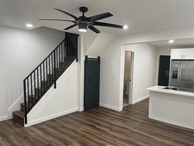 unfurnished living room featuring a barn door, dark hardwood / wood-style floors, and ceiling fan