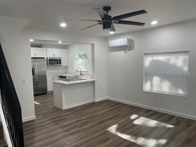 kitchen with kitchen peninsula, dark hardwood / wood-style floors, white cabinetry, appliances with stainless steel finishes, and a wall mounted air conditioner