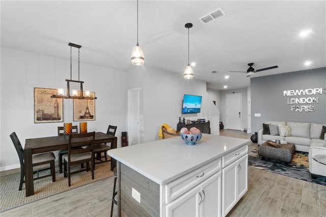 kitchen featuring white cabinets, a kitchen island, light hardwood / wood-style flooring, decorative light fixtures, and ceiling fan with notable chandelier