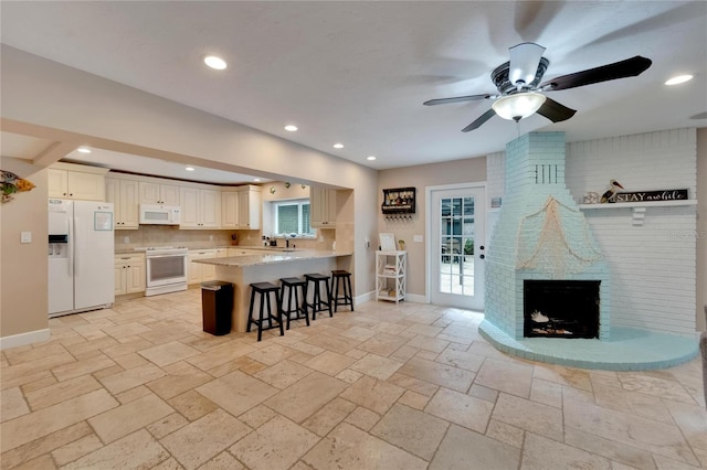 kitchen with a breakfast bar area, kitchen peninsula, a brick fireplace, white appliances, and ceiling fan