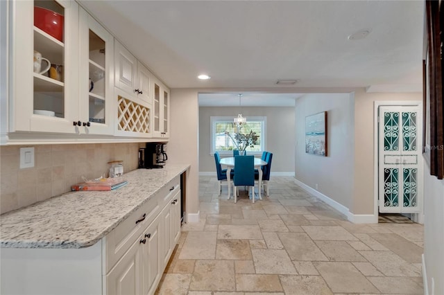 kitchen featuring light stone counters, white cabinets, hanging light fixtures, and tasteful backsplash