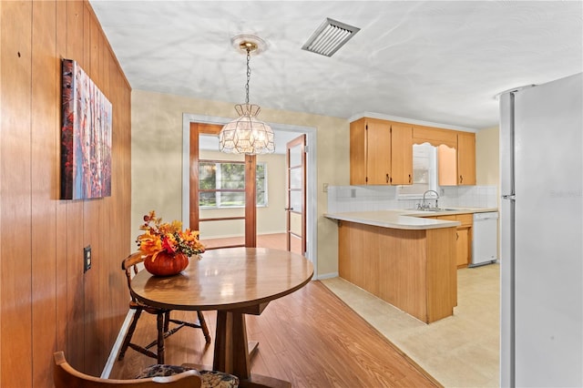 kitchen with kitchen peninsula, light hardwood / wood-style flooring, decorative light fixtures, white dishwasher, and stainless steel fridge