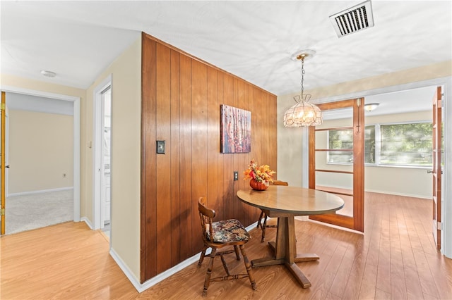 dining room featuring light wood-type flooring, wood walls, and a chandelier