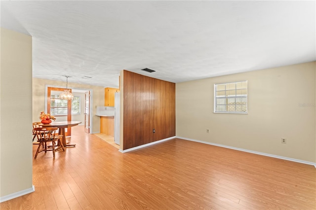 empty room with a notable chandelier, light wood-type flooring, and plenty of natural light