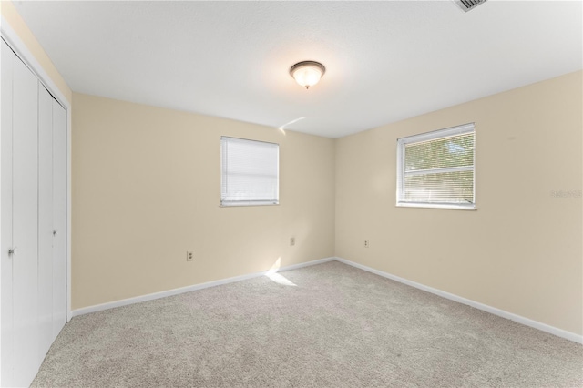 unfurnished bedroom with multiple windows, light carpet, and a closet