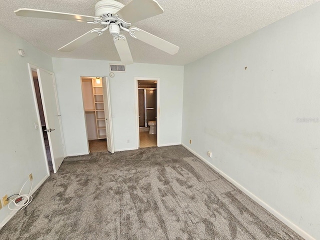 unfurnished bedroom with connected bathroom, a walk in closet, a textured ceiling, carpet flooring, and ceiling fan