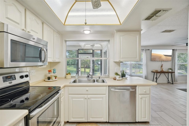 kitchen with white cabinetry, sink, kitchen peninsula, appliances with stainless steel finishes, and light hardwood / wood-style flooring