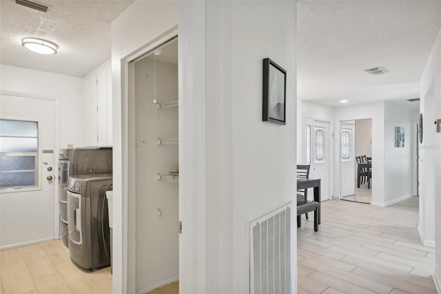 corridor featuring light wood-type flooring, a textured ceiling, and washing machine and clothes dryer