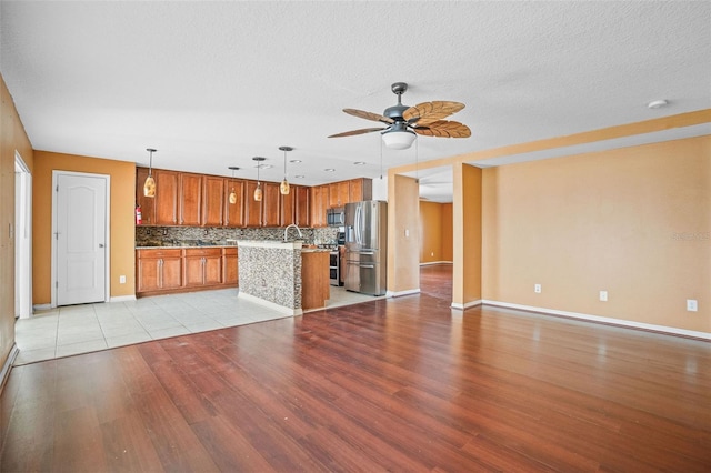 unfurnished living room with a textured ceiling, light hardwood / wood-style floors, ceiling fan, and sink