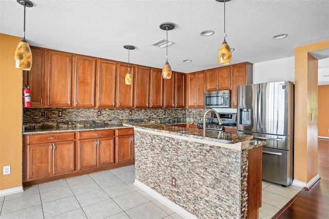 kitchen with pendant lighting, stainless steel appliances, a center island with sink, and a textured ceiling