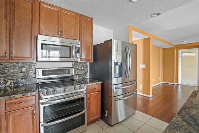 kitchen with dark stone counters, decorative backsplash, light hardwood / wood-style flooring, and stainless steel appliances