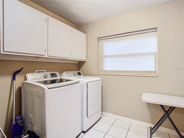 clothes washing area featuring a textured ceiling, washing machine and dryer, light tile patterned floors, and cabinets