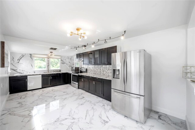 kitchen with light stone counters, sink, stainless steel appliances, a notable chandelier, and decorative backsplash