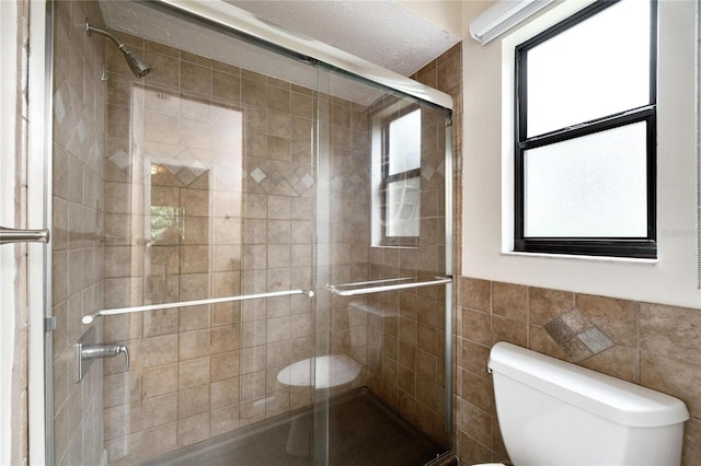 bathroom featuring tile walls, a shower with shower door, toilet, and plenty of natural light